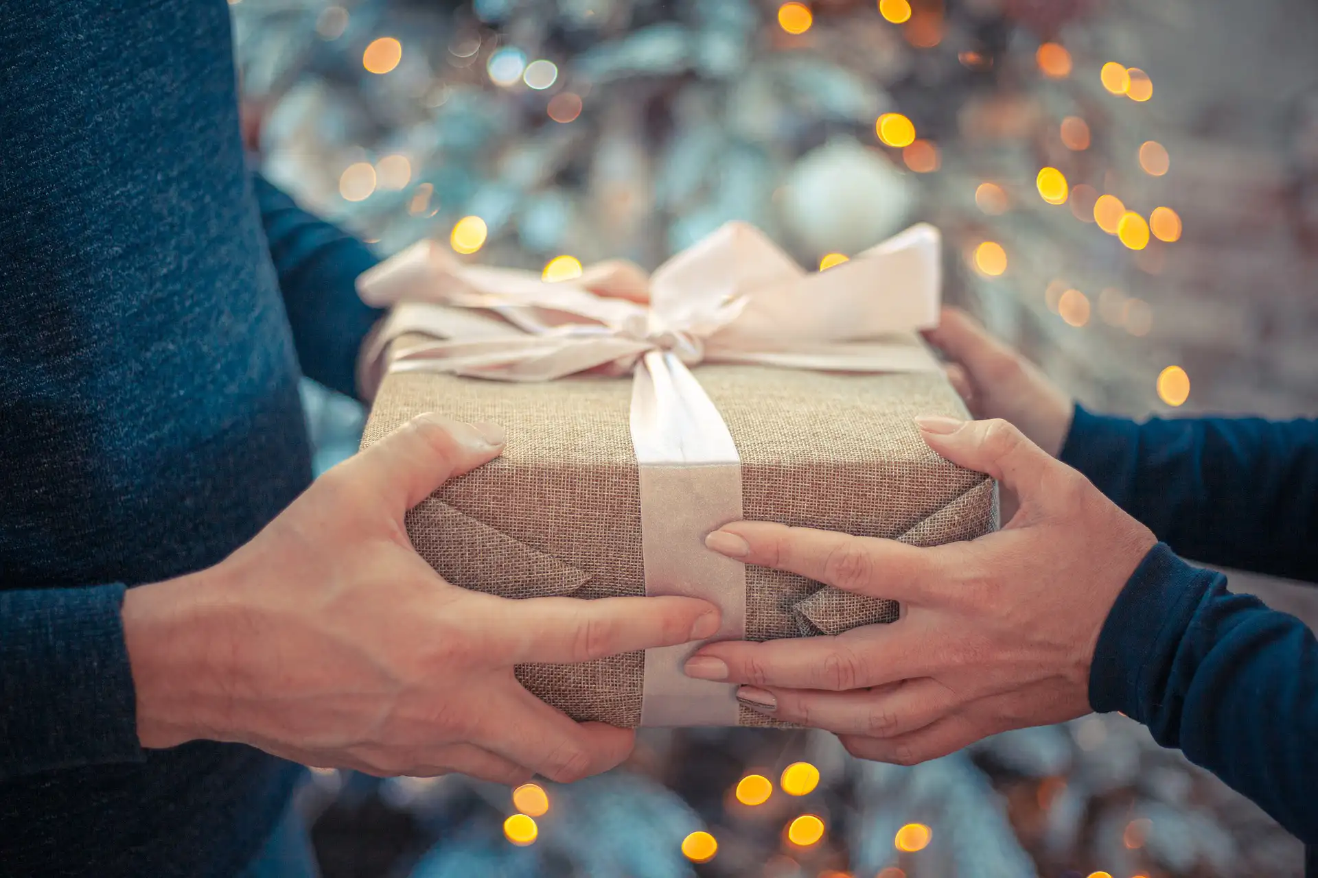 Nell'immagine, un primo piano sulle mani di due persone che si stanno scambiando un pacco regalo.