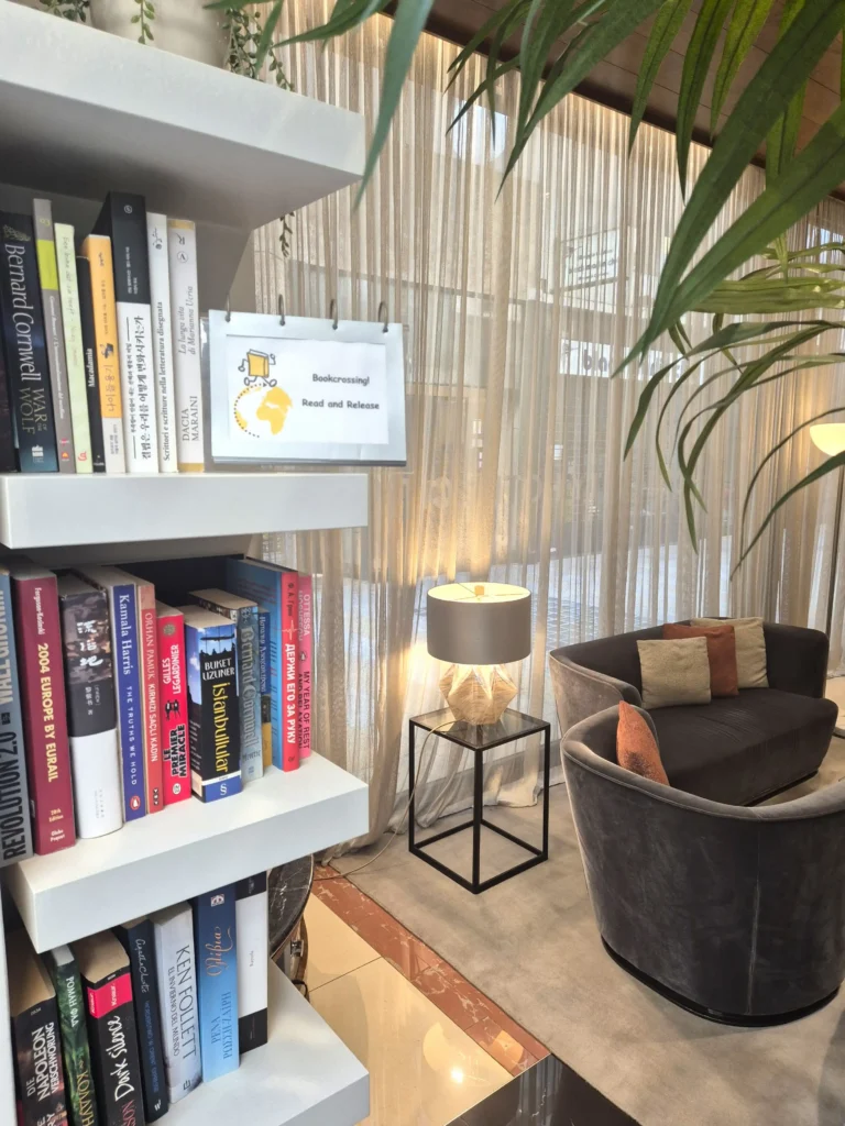 Nell'immagine, una libreria con dei libri a disposizione dei clienti presso l'Hotel City Milano. Sulla destra, si intravede un salottino con poltrone e divanetti.
