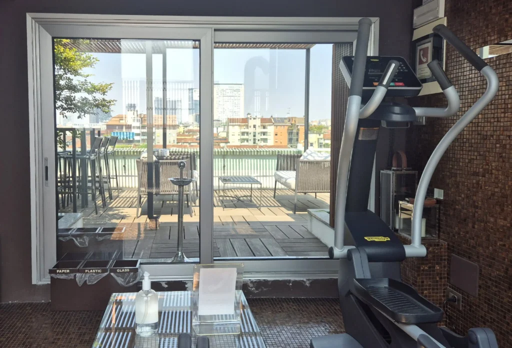 Nell'immagine, la zona fitness dell'Hotel City Milano con un'ellittica TechnoGym. Di fronte, c'è la terrazza con vista sulla città.