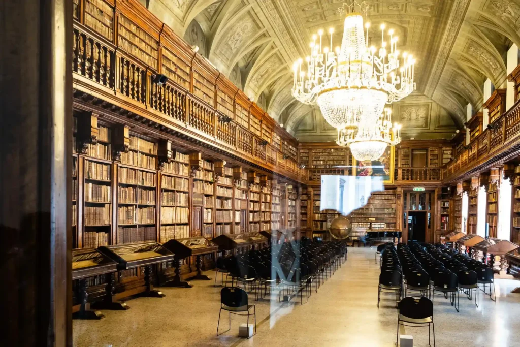 Nell'immagine, una sala della Pinacoteca di Brera a Milano, con un'enorme libreria e alcune file di sedie a centro sala.