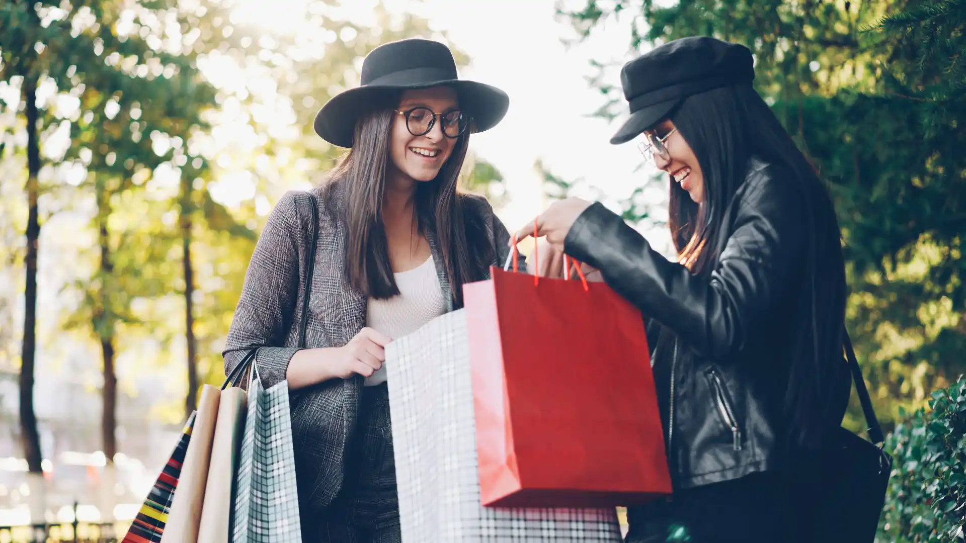 In the picture, two women smilingly look inside some bags after shopping.
